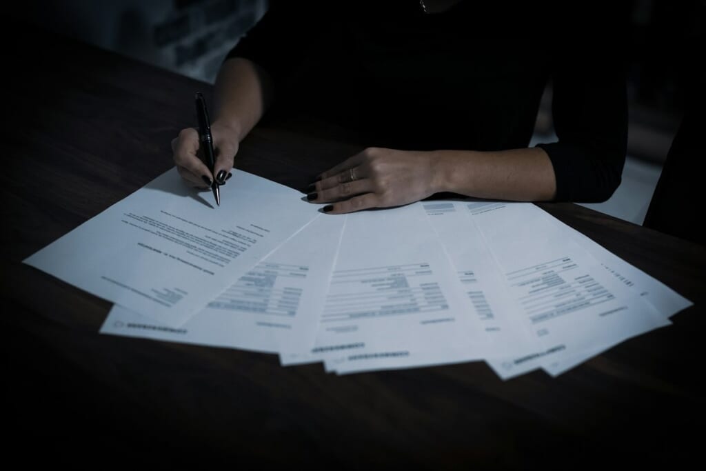 Hands filling in documents spread across a desk